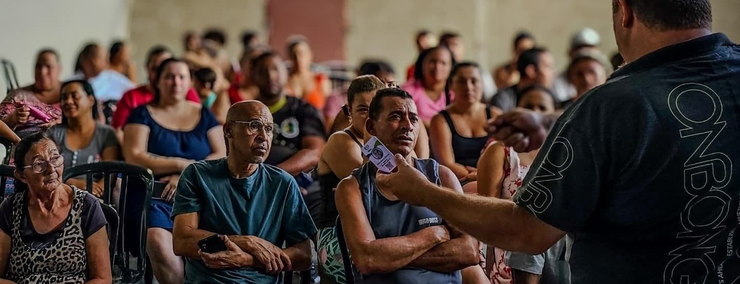 Assembleia do Instituto AMEAS: dezenas de moradores sentados acompanham a fala de um voluntário no salão da sede.