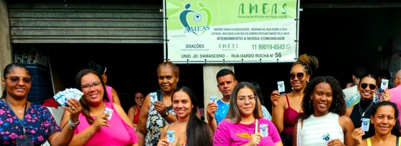 Moradoras reunidas diante da faixa do Instituto AMEAS na sede, que traz o endereço e o telefone de atendimento.