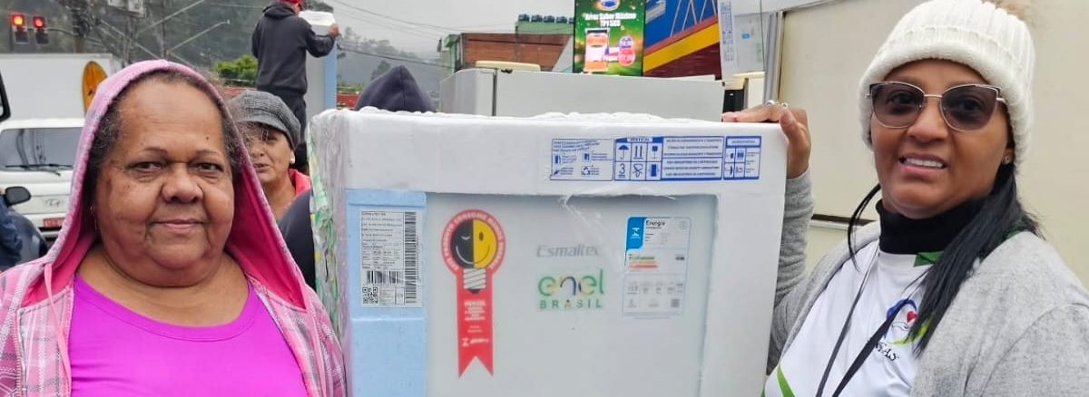 Moradora recebe um refrigerador ao lado de uma voluntária do Instituto AMEAS em ação de apoio habitacional.