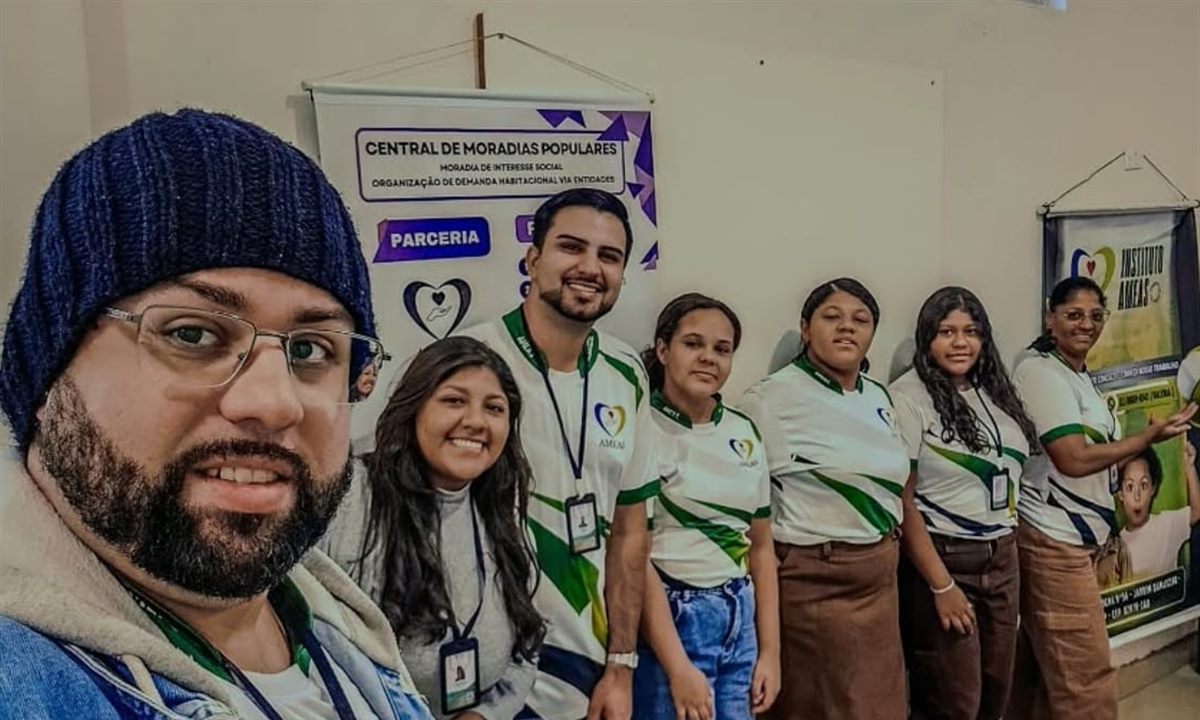 Equipe do Instituto AMEAS uniformizada, reunida na sede diante das faixas da instituição e do programa Central de Moradias Populares.